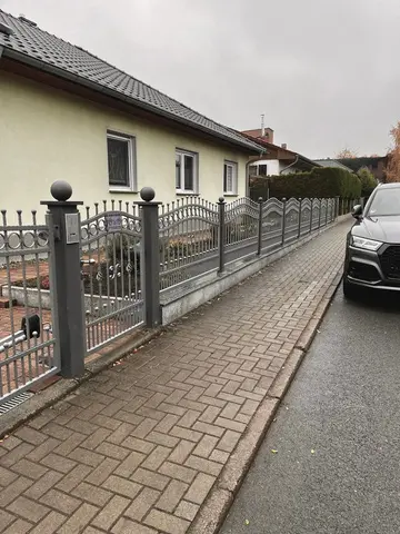 Klassischer Schmiedezaun mit Bögen und dekorativen Elementen vor einem Wohnhaus